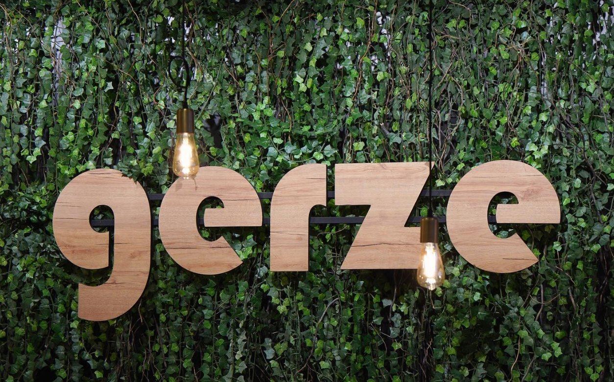 Der Holzschriftzug „gerze“ mit zwei Glühbirnen vor der Efeuwand im Laden
